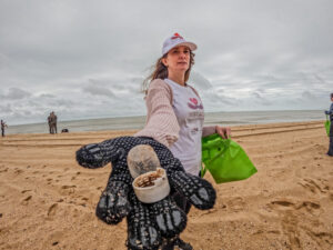 Voluntária recolhendo lixo das areias do mar e a Lagoa de Iquipari