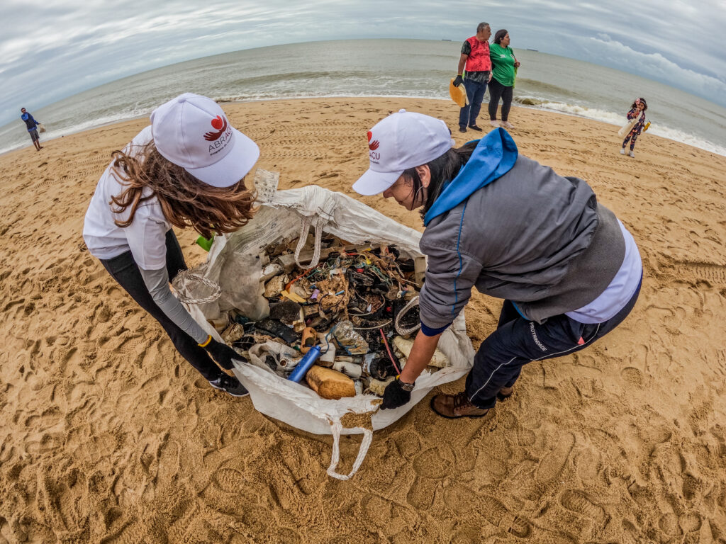 duas mulheres, voluntárias do projeto AbrAçu, recolhendo lixo do mar e a Lagoa de Iquipari
